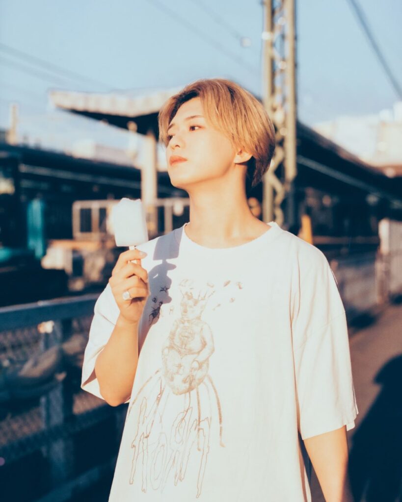 アーティストくじらのプロフィール写真。白いTシャツ姿で夕暮れの駅のホームに立つ爽やかな雰囲気のクリエイター